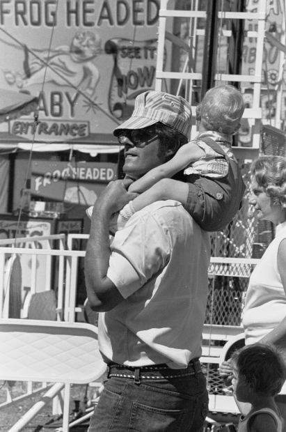 Man with child near sideshow, 1976